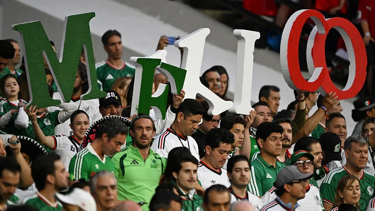 Mexican fans holding letters that spell Mexico cheering at a football stadium.